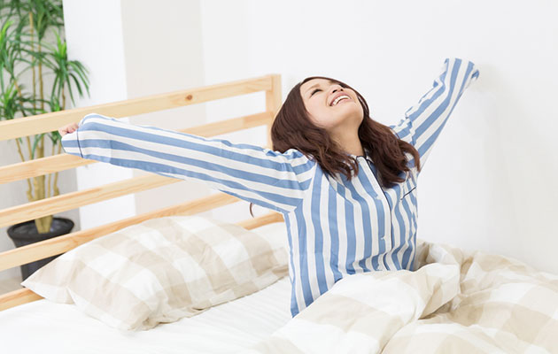 Woman in bed arms outstretched having had a great night's sleep
