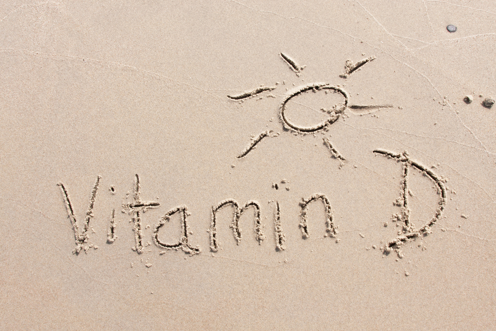 Vitamin D and a sun written into the sand on a beach